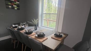 Un comedor con una mesa dispuesta para cuatro, sillas de madera y una ventana con vistas a árboles.
