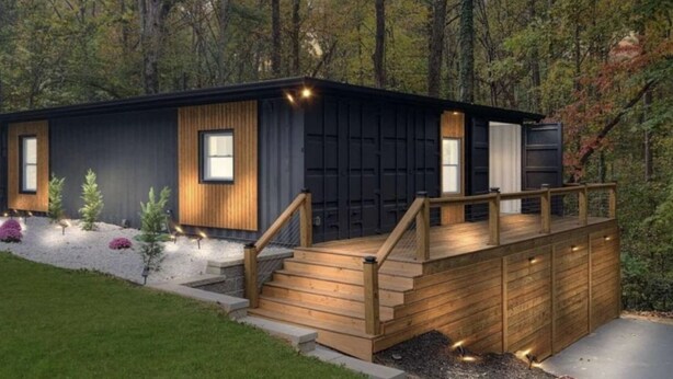 A modern cabin with a wooden deck, a garage, and a landscaped garden.