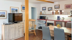 Cocina moderna con televisor, microondas y cafetera. Hay una zona de comedor con mesa y sillas.