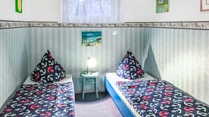 Una habitación con dos camas individuales, cada una con almohadas estampadas, una mesita y una ventana con cortinas translúcidas.