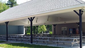 A covered picnic area with benches and a building in the background. - Beautiful Summer village cottage close to the Ocean! (Wells)