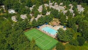 An aerial view of a residential area with a swimming pool surrounded by lounge chairs and umbrellas, tennis courts, and houses. - Beautiful Summer village cottage close to the Ocean! (Wells)