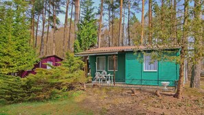 Une petite cabane verte, dotée d’un porche et d’une table, entourée de grands arbres.