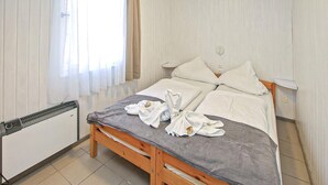 Un lit bien fait, avec du linge de lit et des serviettes blanches, une table de chevet avec une lampe et une fenêtre avec des rideaux.