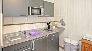 Une cuisine de taille réduite équipée d’un four à micro-ondes, d’un évier et de deux poubelles.