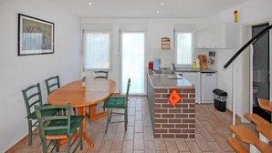 Een kleine keuken met een eethoek, met een houten tafel en stoelen, een keukeneiland van baksteen en witte kastjes.