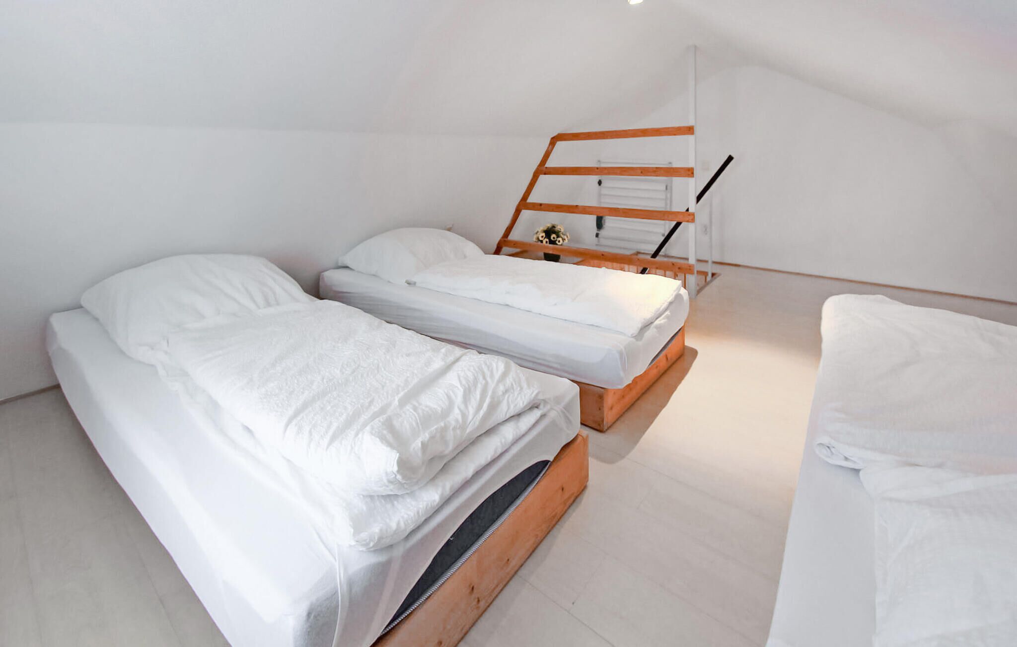 Une petite pièce propre, avec deux lits superposés en bois, du linge de lit blanc et un plafond blanc.