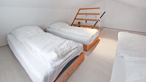 Een kleine, schone kamer met twee houten stapelbedden, wit beddengoed en een wit plafond.