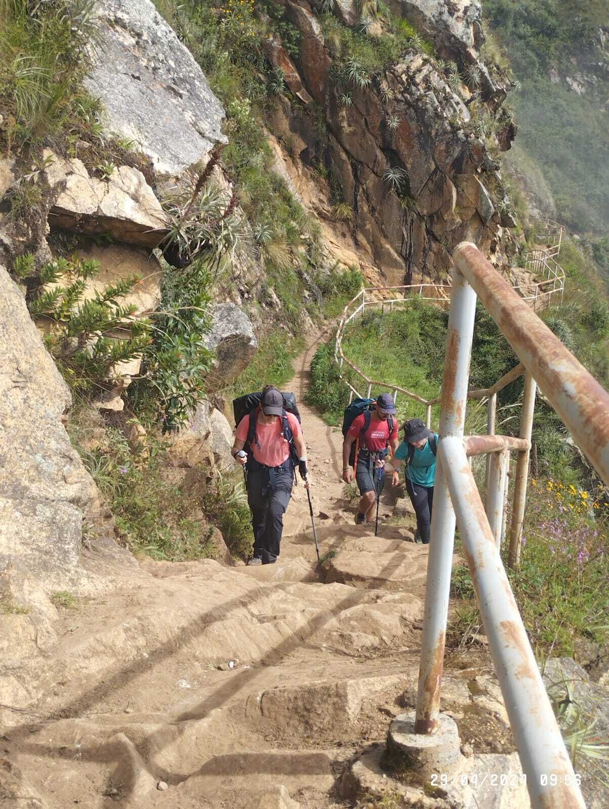 A rocky hiking trail with metal railings and hikers using trekking poles.