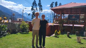 Two people standing in front of a wooden house with a sign indicating it is a hotel. - the wooden house choquequirao (San Pedro de Cachora)