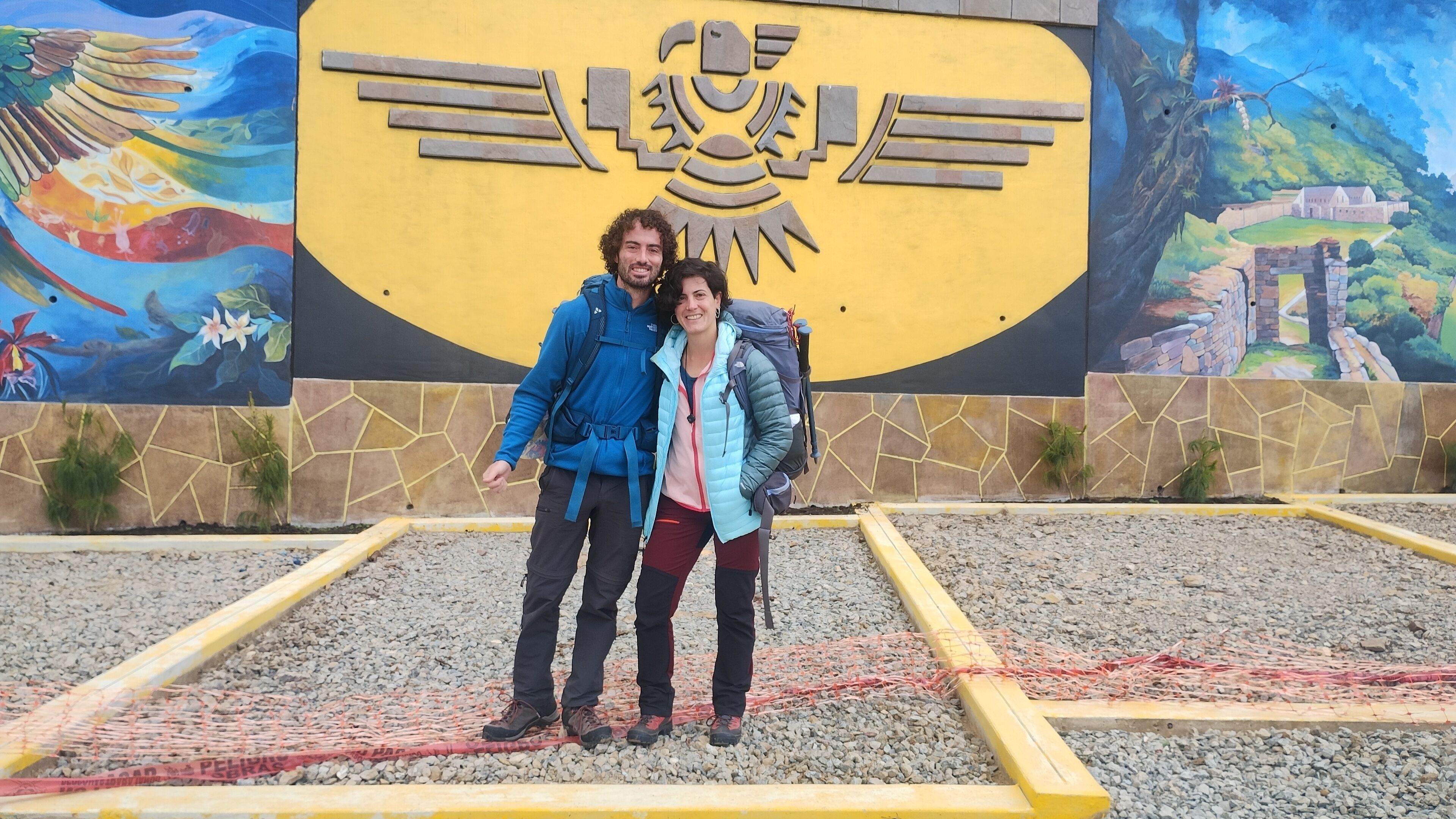 Two people standing in front of a mural with a yellow background and a castle illustration.
