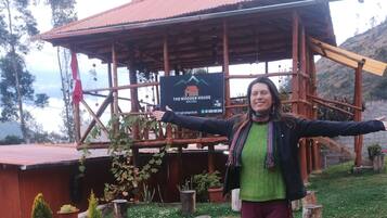 Una casa de madera con techo rojo, rodeada de vegetación y un letrero que indica que es un albergue.