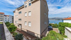 A multi-story building with a flat roof, white window shutters, and a view of a body of water and distant hills.