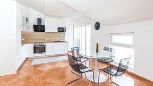 A modern kitchen with white cabinets, a built-in oven, and a microwave. There is a glass dining table with four chairs.