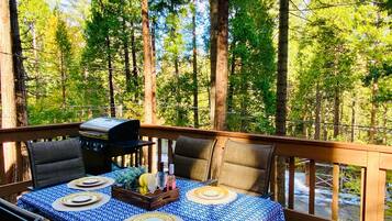 An outdoor deck with a table set for dining, surrounded by tall trees.