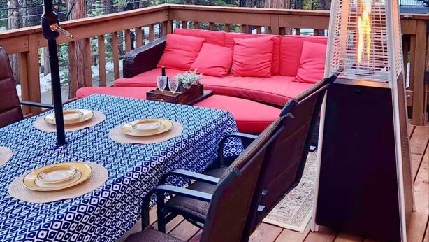 A deck with a red umbrella, a sofa, and a table set for dining.
