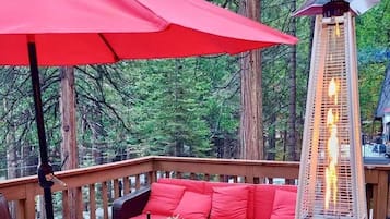 A deck with a red umbrella, a sofa, and a table set for dining.