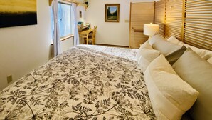 A bedroom with a large bed, a desk, and a window with curtains.