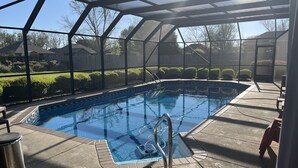 Una piscina techada al aire libre con agua azul cristalina, rodeada por un deck pavimentado y una cerca metálica.