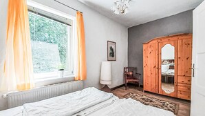 Une chambre à coucher avec un lit, une armoire en bois, une chaise, un radiateur et une fenêtre avec des rideaux.