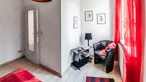Une pièce avec une porte, une petite table avec une lampe, une chaise et un rideau rouge.