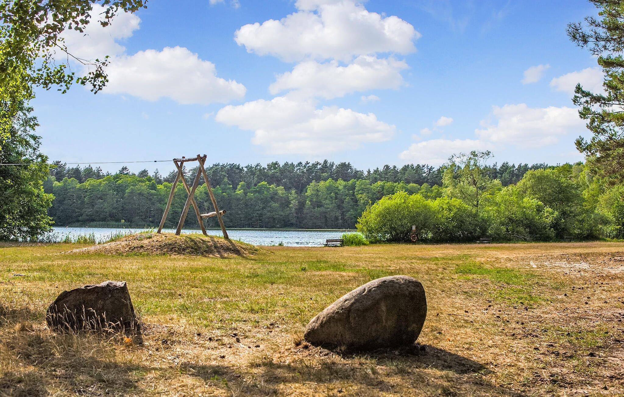 Eine natürliche Landschaft mit einer Schaukel, einer Bank und einem großen Felsen im Vordergrund.