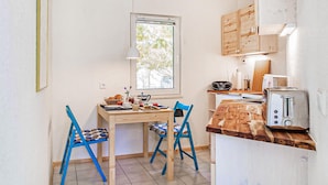 A small kitchen with a wooden table, two blue chairs, a window, and basic appliances. - Ferienwohnung Rheinsberg (Rheinsberg OT Kagar)
