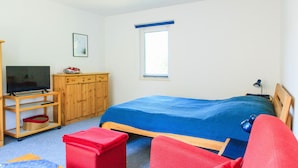 A bedroom with a bed, a TV, a wardrobe, a window, and a desk with a lamp. - Ferienwohnung Rheinsberg (Rheinsberg OT Kagar)