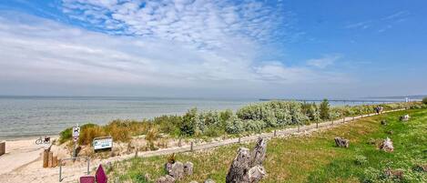 A coastal path with a view of the sea, wooden posts, and a signboard.