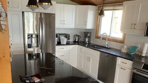 Uma cozinha moderna com armários brancos, eletrodomésticos de aço inoxidável, bancada preta e dois banquetes pretos.
