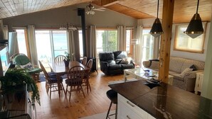 Uma sala ampla com mesa de jantar, cadeiras, sofá e cozinha, incluindo bancada e armários.