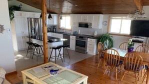 Ampla sala de estar com mesa de jantar de madeira, sofá e cozinha ao fundo.