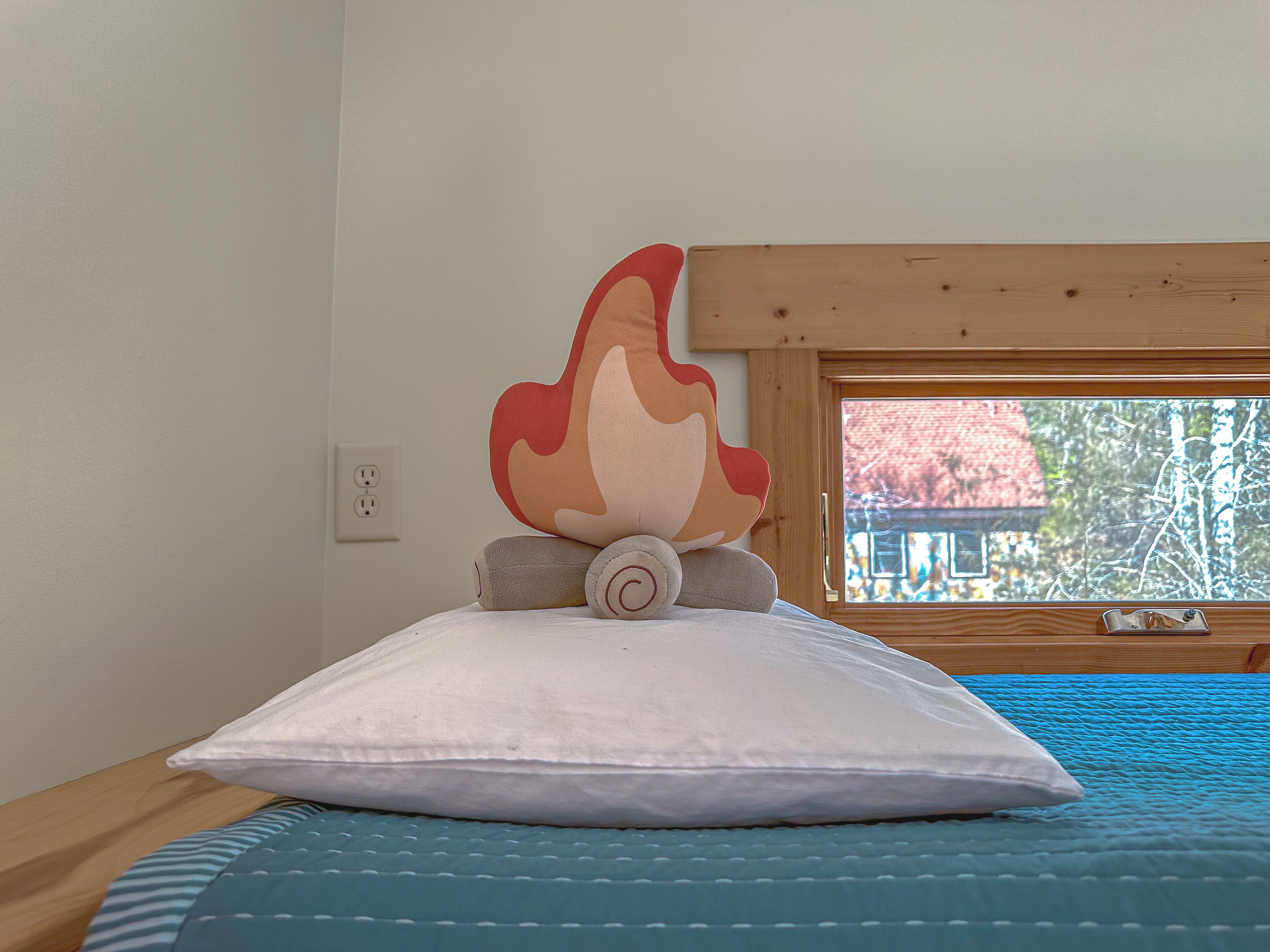 Una cama con un almohadón blanco, una manta azul a rayas y un cojín decorativo grande con diseño de llama.