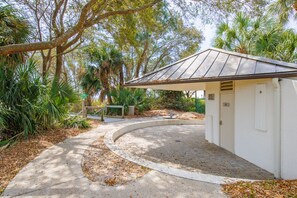 A small, white building with a metal roof, surrounded by trees and a paved path. - 3086 Seascape Villa @ Forest Beach | Lagoon View | Pool & Large Outdoor Space (Hilton Head Island)
