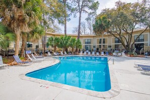Une piscine entourée de chaises longues et de palmiers, le tout bordé par un bâtiment doté de nombreuses fenêtres et de balcons.
