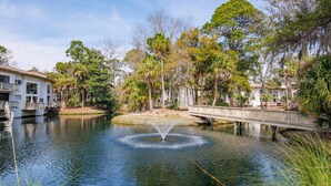 Une scène paisible au bord de la rivière, avec un pont, une fontaine et un bâtiment doté de balcons.