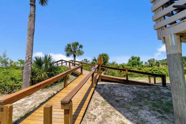 A wooden boardwalk leading to a beach area with palm trees and a clear blue sky.