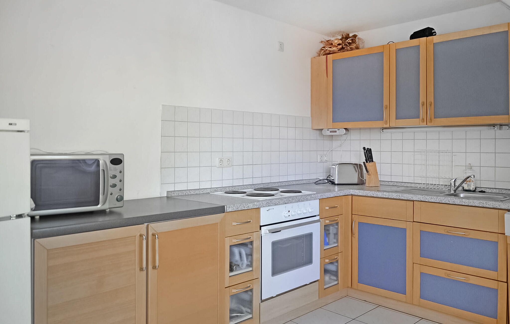 Une cuisine compacte équipée d’un four à micro-ondes, d’une cuisinière et d’un four, de placards en bois et d’un pare-feu en carreaux.