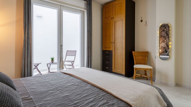 A bedroom with a bed, a wardrobe, a chair, and a balcony. - GuestHost - Wonderful villa that comfortably accommodates 8 people in 185 m2, with four bedrooms, three bathrooms and 40 m2 of outdoor area equipped for moments of relaxation. The modern furnishings but with natural inspirations create a heavenly and rel (Bari)