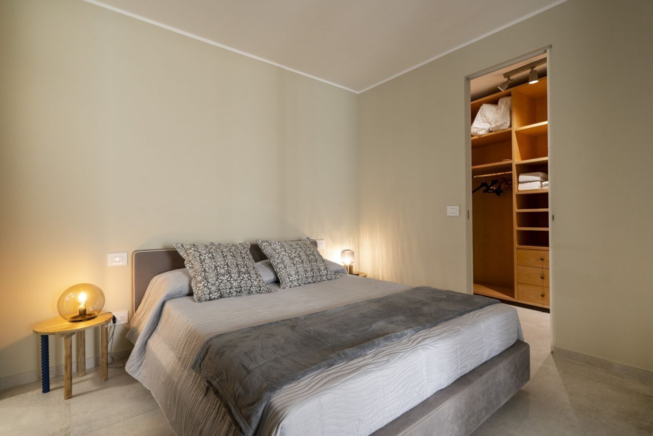 Un dormitorio con cama, lámparas de noche, armario y mesita de noche.