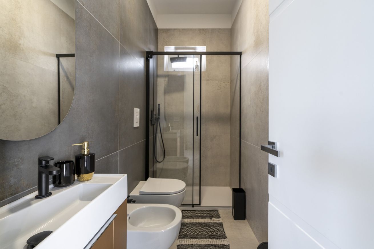 Une salle de bain moderne avec une douche à parois de verre, un lavabo blanc doté de robinetterie noire et un bidet.