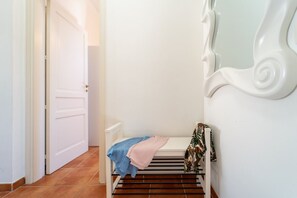 A hallway with a white door, a bench with a blue and pink blanket, and a white wall with a decorative molding.