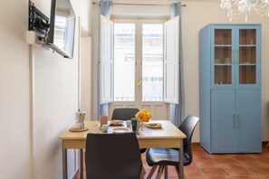 Un coin repas avec une table dressée pour deux personnes, un buffet bleu et une fenêtre avec des rideaux.