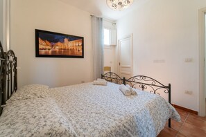 A bedroom with a bed, a painting on the wall, and a window with curtains.