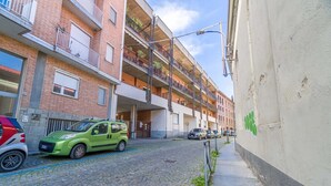 A multi-story residential building with a brick facade, balconies with plants, and a cobblestone street. - GuestHost - Modern and functional apartment of approximately 50 m2, ideal for 3 people, is located on the third floor of a period building equipped with a lift and consists of a kitchenette, living area, a bedroom, a bathroom and two balconies. We are in (Asti)