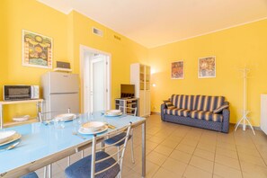 A compact living space with a dining table, chairs, a sofa, a television, and a refrigerator. - GuestHost - Modern and functional apartment of approximately 50 m2, ideal for 3 people, is located on the third floor of a period building equipped with a lift and consists of a kitchenette, living area, a bedroom, a bathroom and two balconies. We are in (Asti)