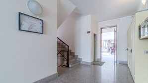 A hallway with a staircase, a framed notice, and a door leading outside. - GuestHost - Modern and functional apartment of approximately 50 m2, ideal for 3 people, is located on the third floor of a period building equipped with a lift and consists of a kitchenette, living area, a bedroom, a bathroom and two balconies. We are in (Asti)