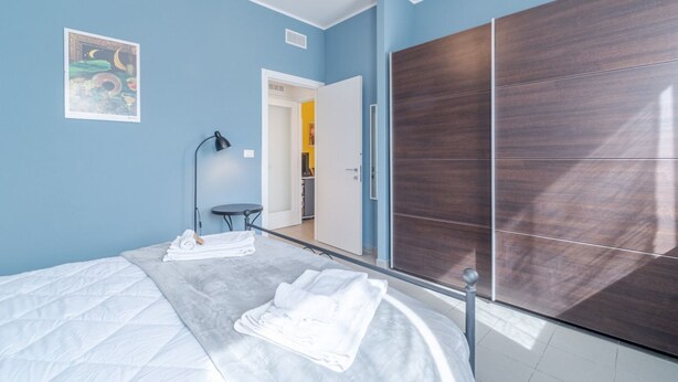 A bedroom with a bed, a wardrobe, a mirror, and a door leading to a bathroom. - GuestHost - Modern and functional apartment of approximately 50 m2, ideal for 3 people, is located on the third floor of a period building equipped with a lift and consists of a kitchenette, living area, a bedroom, a bathroom and two balconies. We are in (Asti)