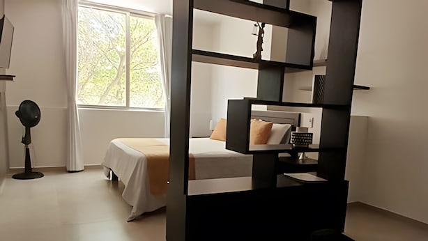 Quarto moderno com cama, escrivaninha e cadeira. Há uma janela com cortinas e vista para árvores.