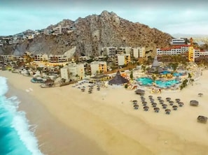 A coastal resort with multiple buildings, a beach, and a mountain backdrop. - 2BDFinisteria Resort Pool & Ocean Views (Cabo San Lucas)